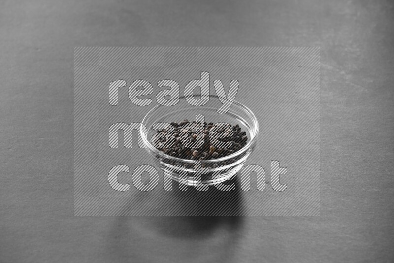 A glass bowl full of black peppers on black flooring