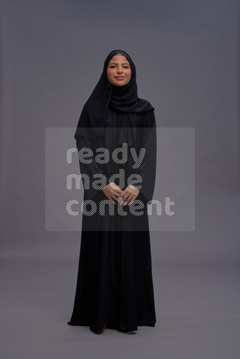 Saudi woman wearing Abaya standing interacting with the camera on gray background