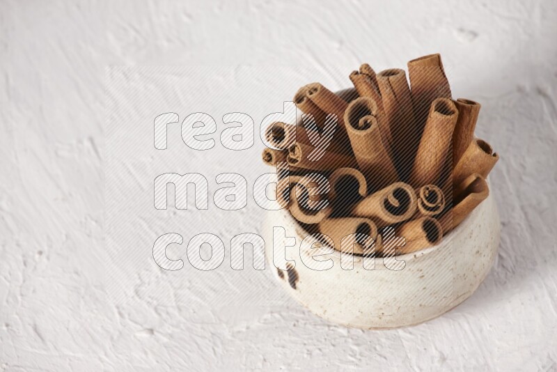 Cinnamon sticks in a beige bowl on a white background