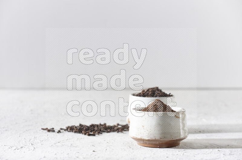 وعاءين من السيراميك بيج اللون، أحدهما مملوء بالقرنفل والآخر مملوء بالبودرة على أرضية بيضاء