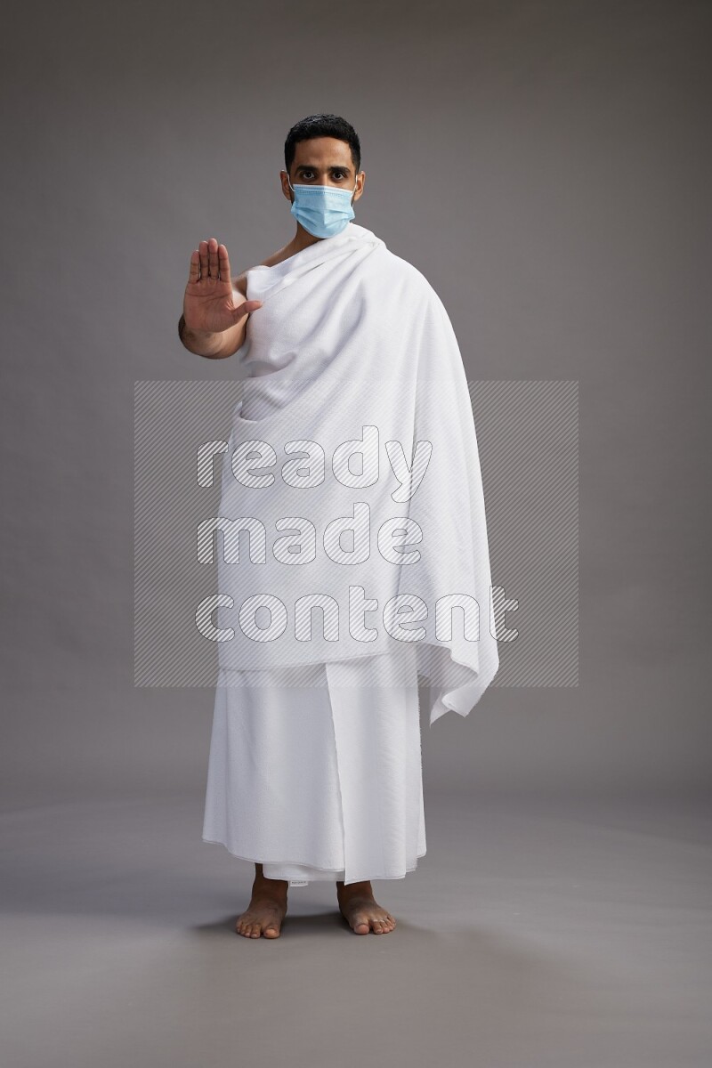A man wearing Ehram with face mask Standing Interacting with the camera on gray background