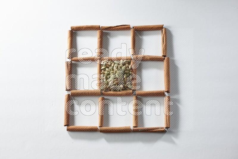 9 مربعات من أعواد القرفة ممتلئة بالهيل في المنتصف محاطة بجوزة الطيب والقرفة وأوراق الغار والقرنفل والكمون والريحان المجفف والزنجبيل المجفف واليانسون النجمي على أرضية بيضاء