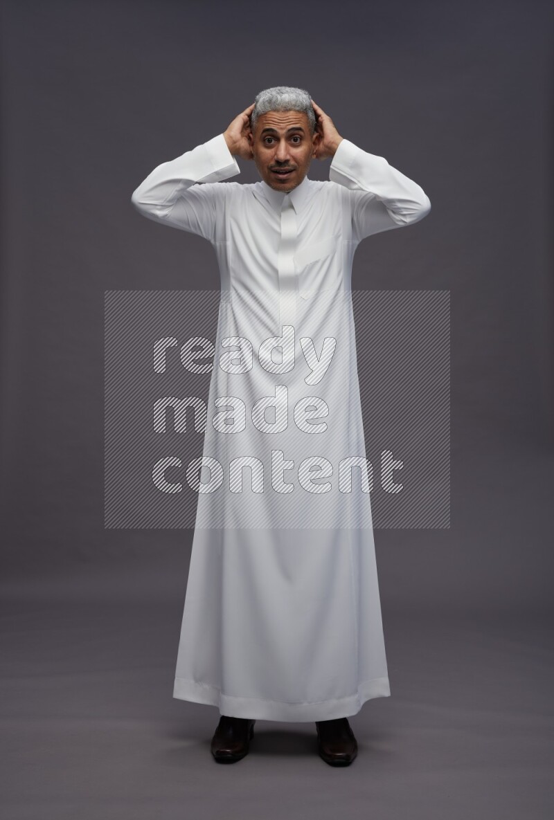 Saudi man wearing thob standing hands behind head on gray background