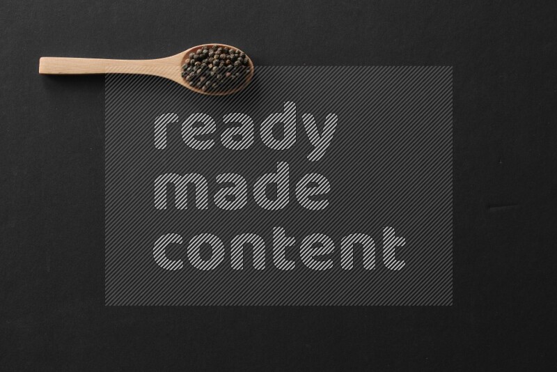 wooden spoons filled with white peppers, cloves, cardamom, salt, black peppers and basil on black flooring