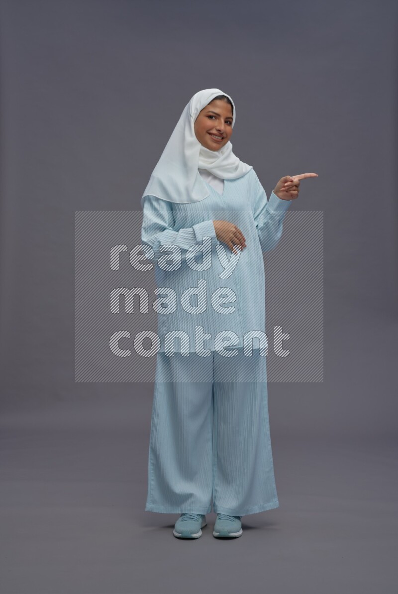 Saudi woman wearing hijab clothes standing interacting with the camera on gray background