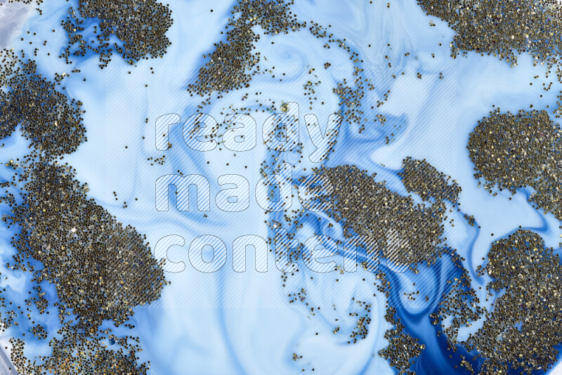 A close-up of sparkling gold glitter scattered on swirling blue background
