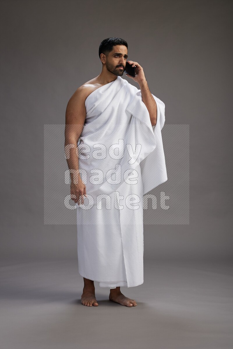 A man wearing Ehram Standing talking on phone on gray background