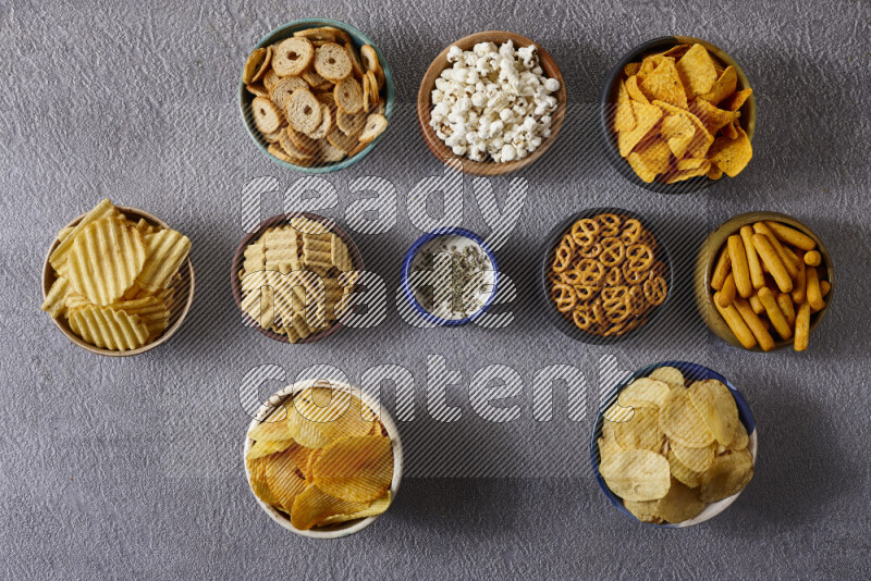 Assorted snacks in pottery bowls on grey background