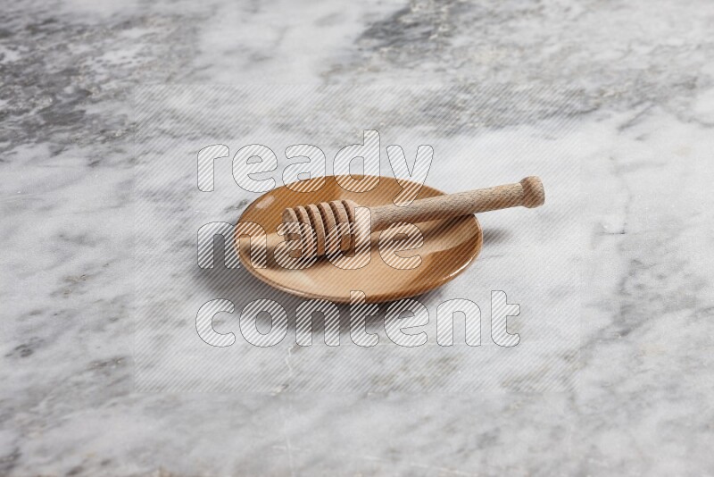Multicolored pottery plate with wooden honey dipper in it on grey marble background