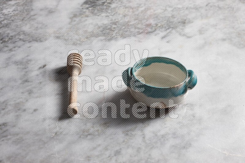 Multicolored pottery bowl with wooden honey dipper on the side on grey marble background