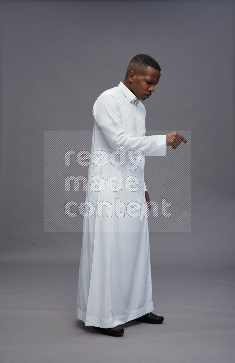 Saudi man wearing thob standing interacting with the camera on gray background