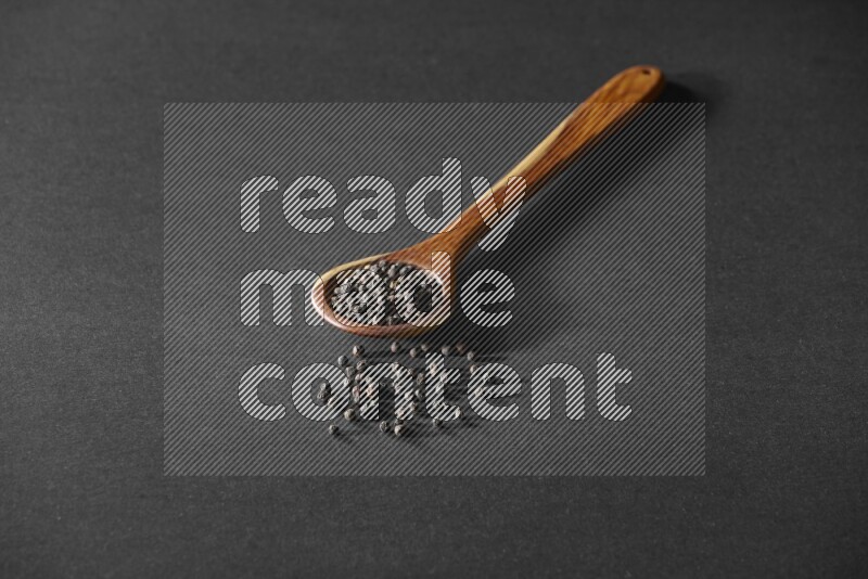 حبوب الفلفل الأسود في مغرفة خشبية علي خلفية سوداء