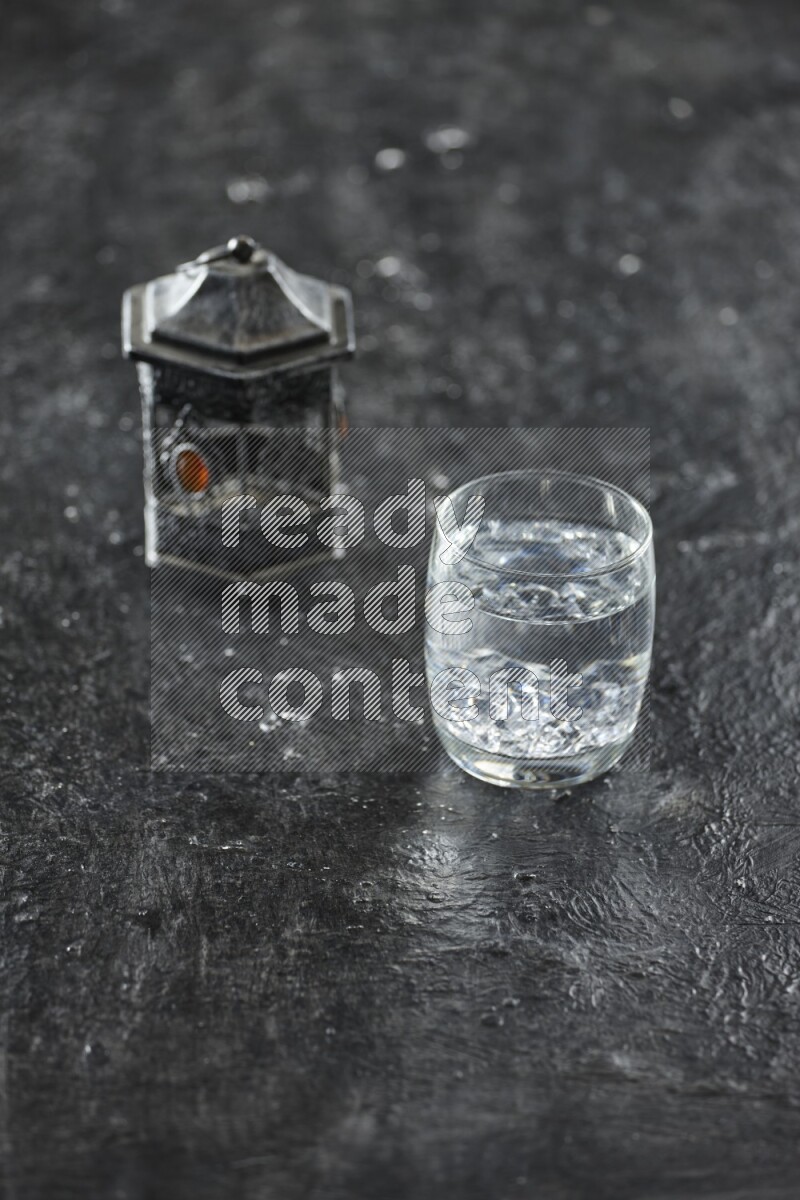 A silver lantern with different drinks, dates, nuts, prayer beads and quran on textured black background