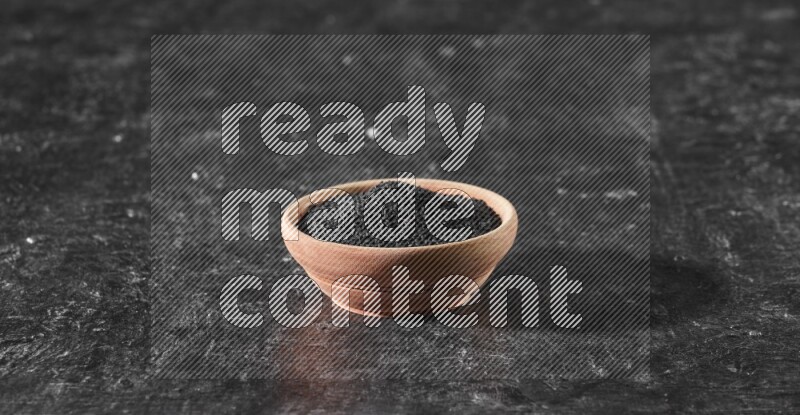 وعاء خشبي ممتلئ ببذور حبة البركة علي خلفية سوداء