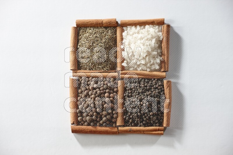 4 مربعات من أعواد القرفة ممتلئة بالكمون والملح الأبيض وبهار الفلفل الحلو وحبوب الفلفل الأسود على أرضية بيضاء