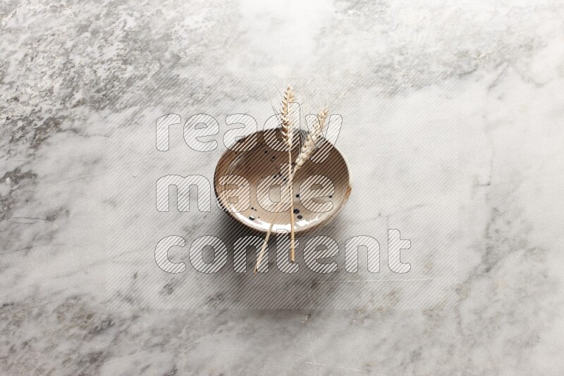Wheat stalks on multicolored pottery bowl on grey marble background