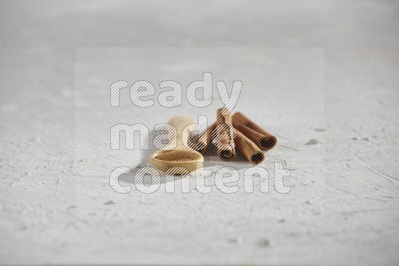 Cinnamon powder in a wooden spoon with cinnamon sticks on white background