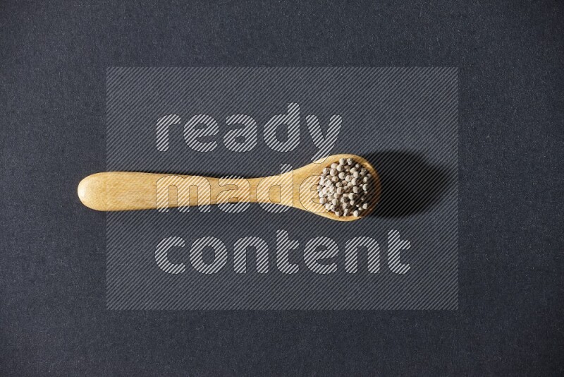 A wooden spoon full of white pepper beads on black flooring